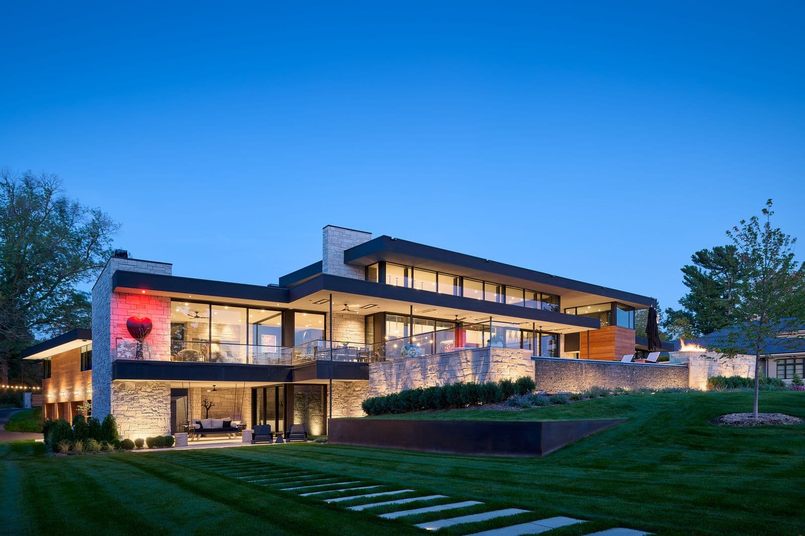 Modern lakefront estate with uplighting on stone walls and fire features