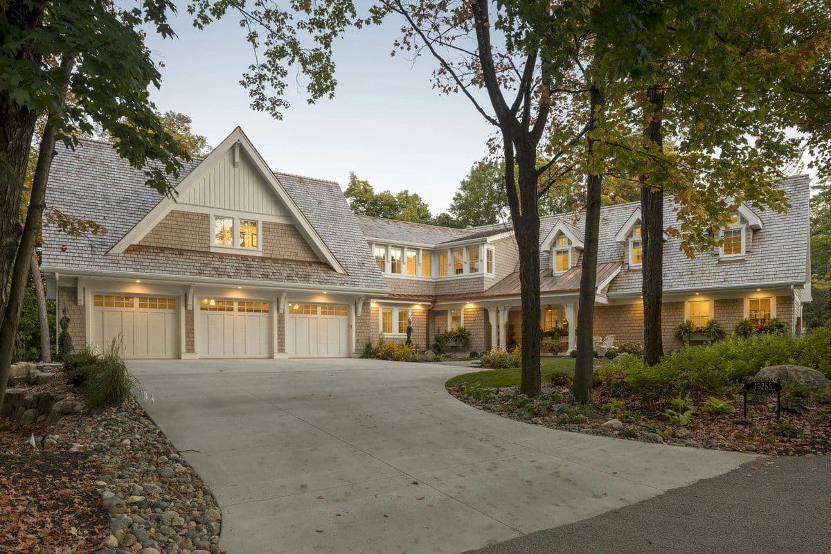 Shingle-style home at twilight with garage and porch lighting